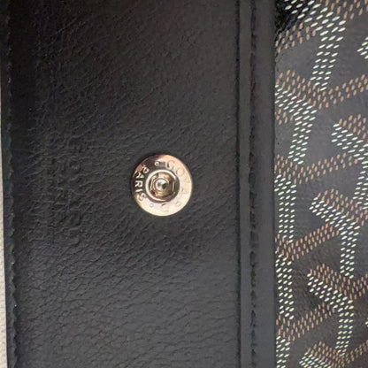 Close-up detail of a luxury handbag showing a black textured leather panel with a silver-tone metal snap button, flanked by a beige vertical stripe and a black-and-gold monogram patterned fabric.