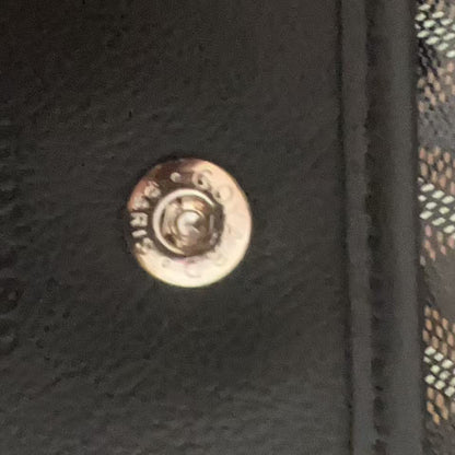 Close-up of a black textured leather or faux-leather surface with a round metallic snap button and part of a brown-and-white patterned textile visible on the right.