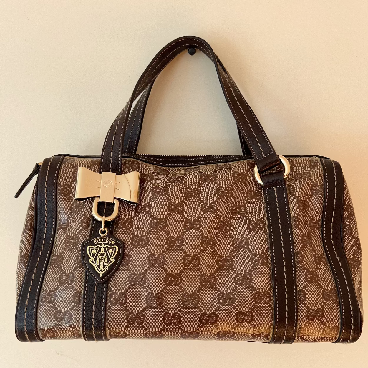 Brown patterned handbag with a gold bow and heart detail on a beige background