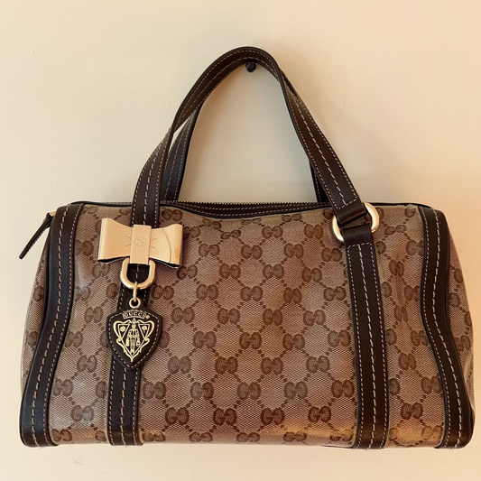 Brown patterned handbag with a gold bow and heart detail on a beige background