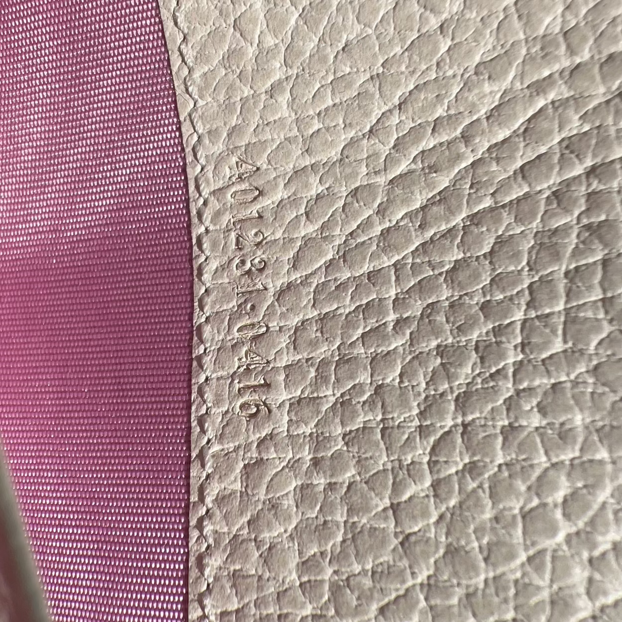 Close-up of textured pink fabric and beige leather surface with visible stitching.