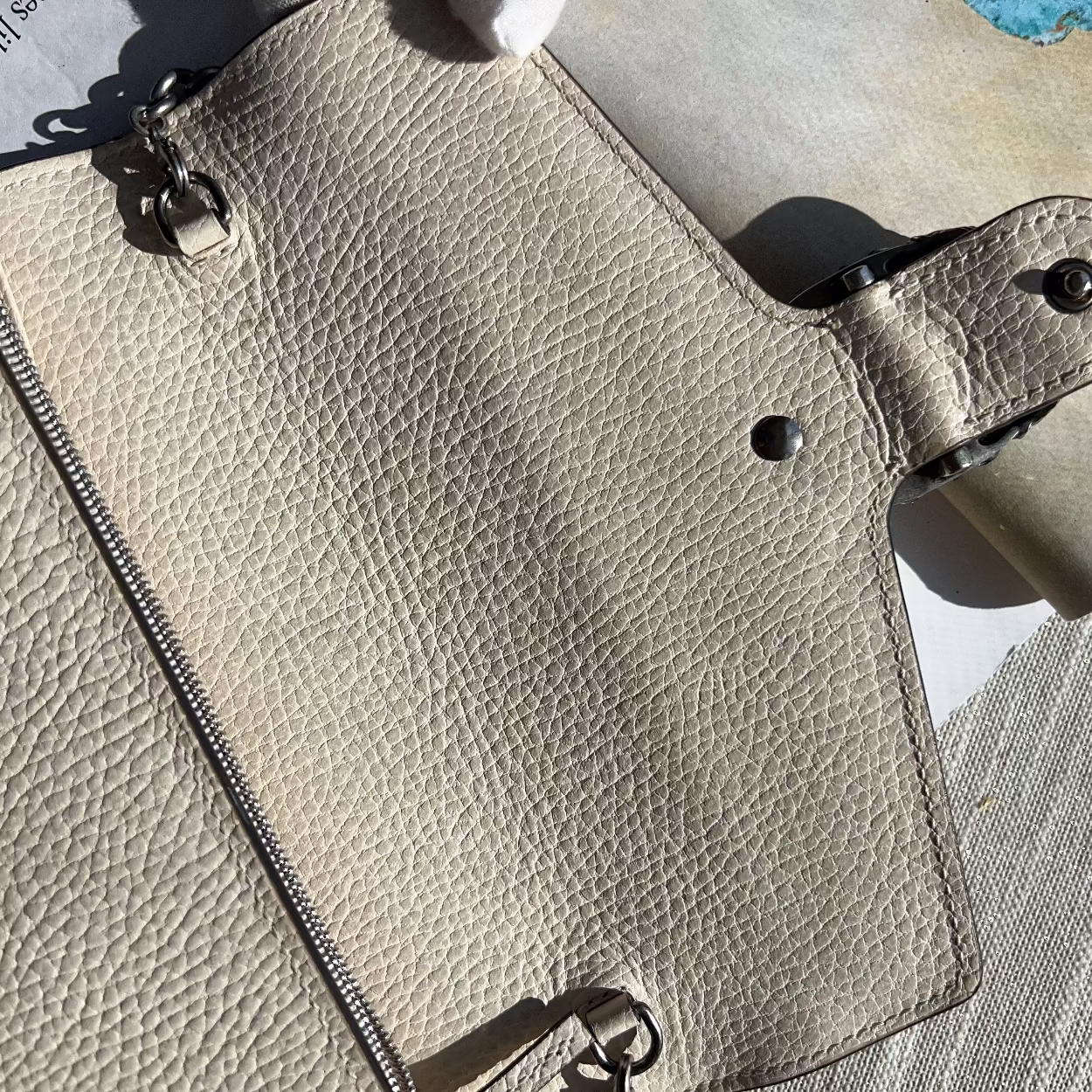Close-up of a beige leather wallet with metal accents on a textured surface.