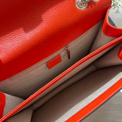Close-up of an open bright orange-red pebbled leather handbag showing the interior lining, zip pocket, and chain hardware.