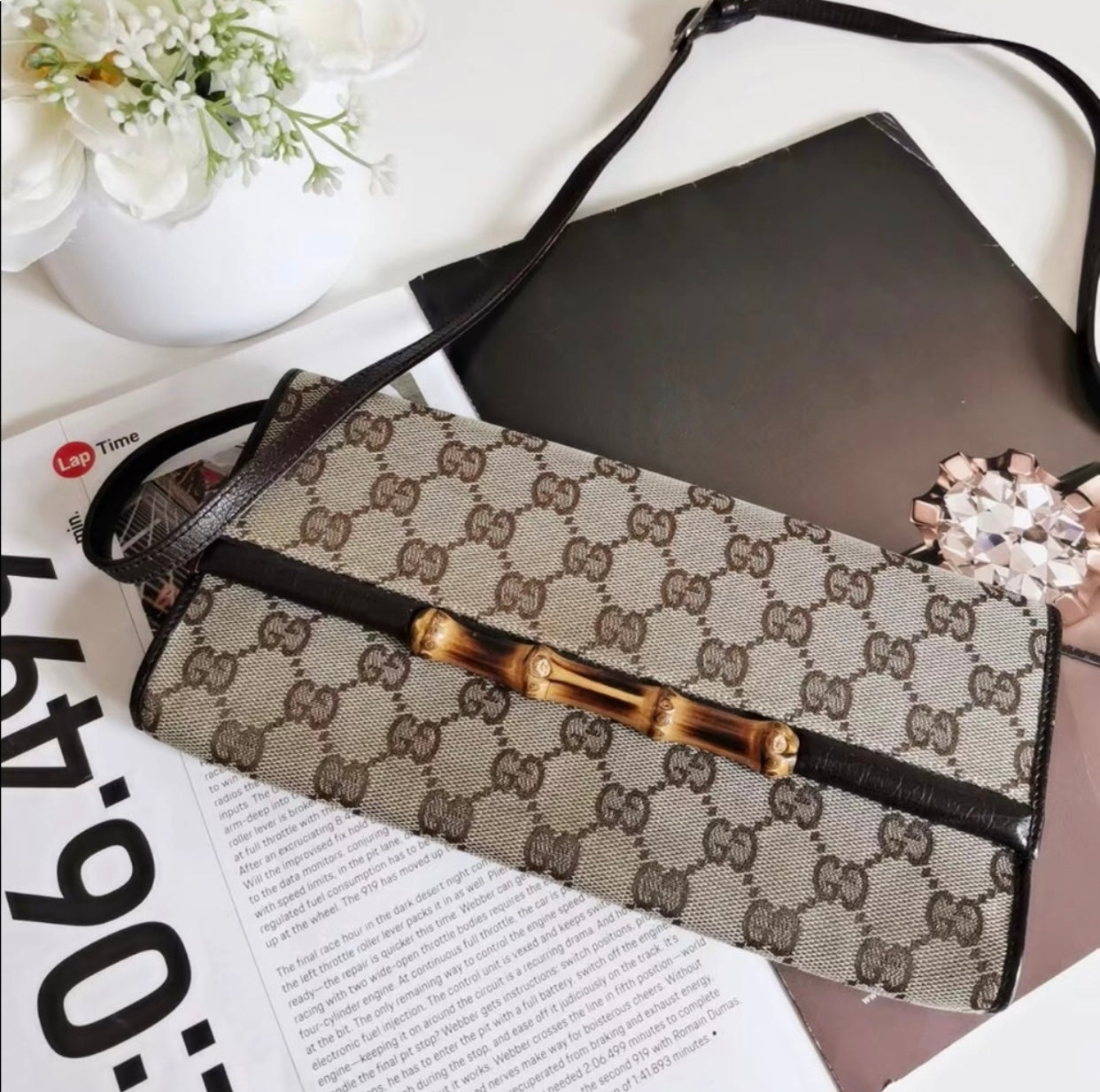 Designer handbag with gold hardware on a magazine with flowers and jewelry in the background