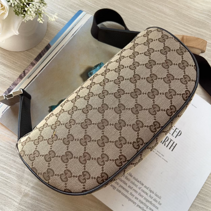A Gucci shoulder bag in the classic GG Supreme monogram canvas, styled on top of an open book with a magazine and a small potted plant nearby.