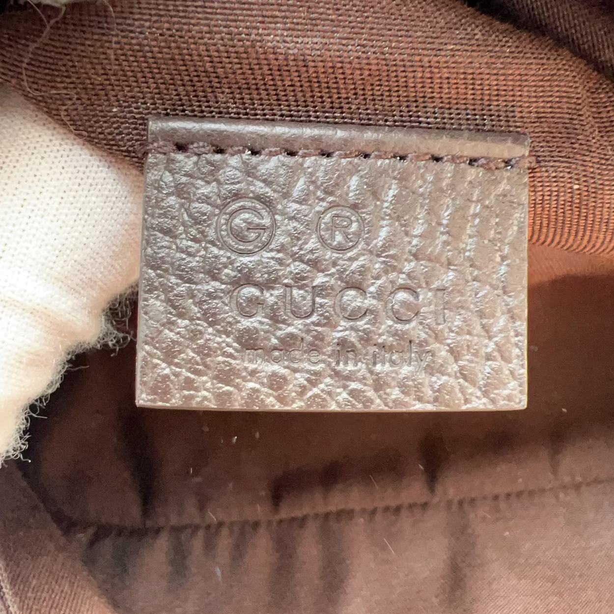 Close-up of a Gucci leather interior label stamped with the brand name and logo, set against brown fabric.