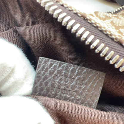 Close-up of a brown textured leather interior label with embossed lettering, held by a white gloved hand near a brown fabric surface and a metallic zipper.