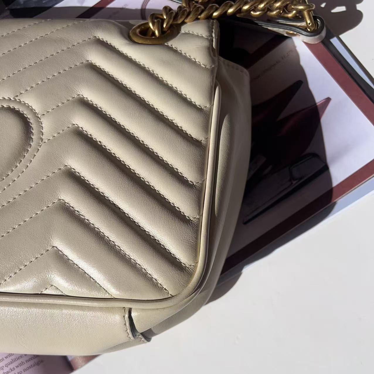 Beige handbag with a gold chain strap on a white surface