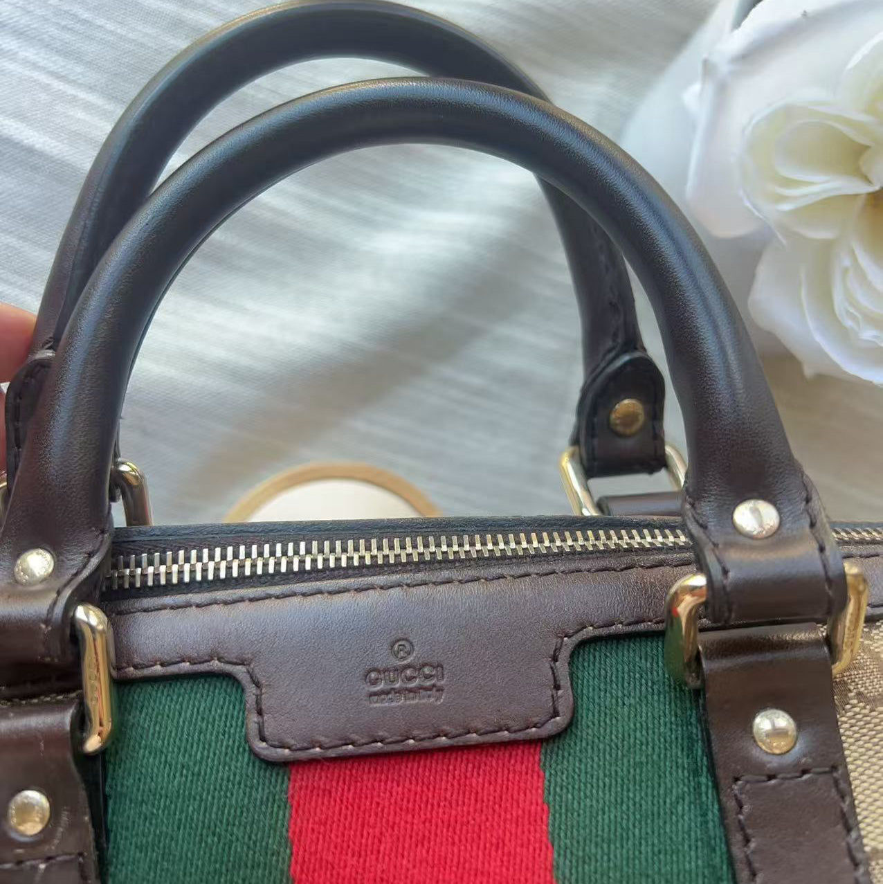 Close-up of a Gucci handbag showing the iconic green and red web stripe canvas, brown leather trim, gold-tone hardware, and the embossed Gucci logo on a leather patch.