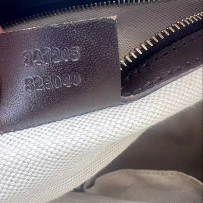 Close-up of a canvas bag interior showing a dark brown leather zipper pull stamped with embossed serial numbers, held by a finger.