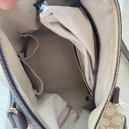 Close-up of the interior of a beige and brown patterned handbag, showing the lining, zipper compartments, and a hand holding the opening.