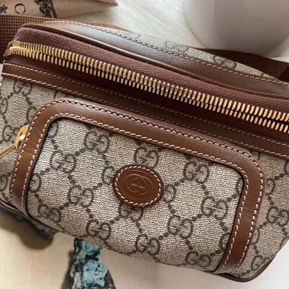 A close-up of a Gucci monogram canvas pouch with brown leather trim and gold-tone zippers, resting on a light surface with decorative stones nearby.