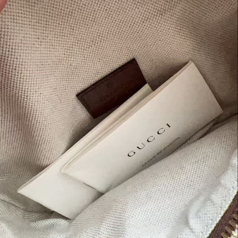 Close-up of the interior of a Gucci pouch or bag, showing beige canvas lining, a brown leather interior trim, gold-tone zipper, and a visible Gucci dust bag inside.