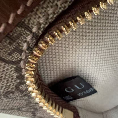 Close-up of a beige woven fabric interior with a gold zipper and a small black brand tag reading GU 10386. A finger is visible at the bottom edge.