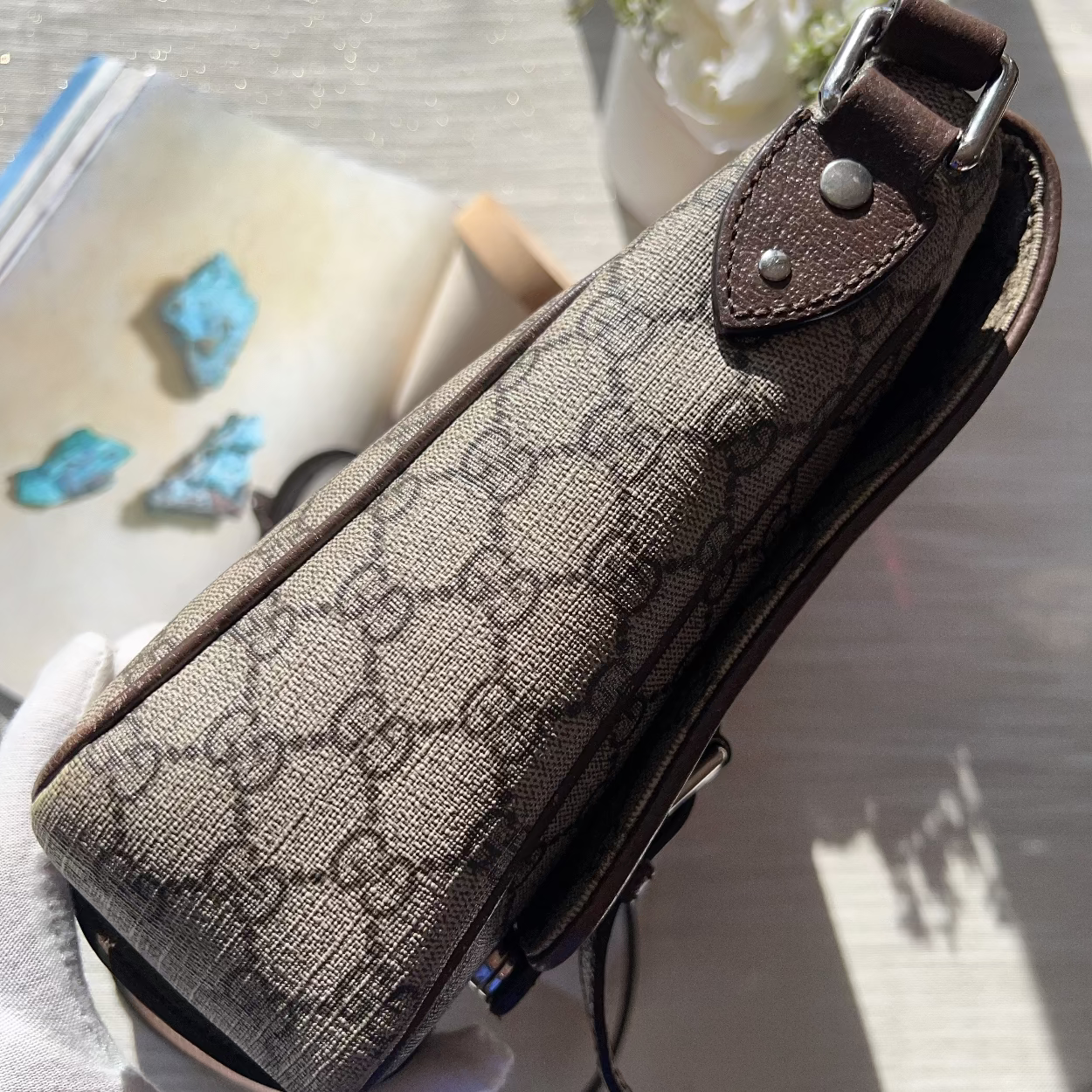 Brown patterned pouch with leather strap held by a person, with a blurred background.