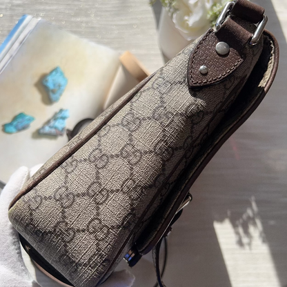 Brown patterned pouch with leather strap held by a person, with a blurred background.