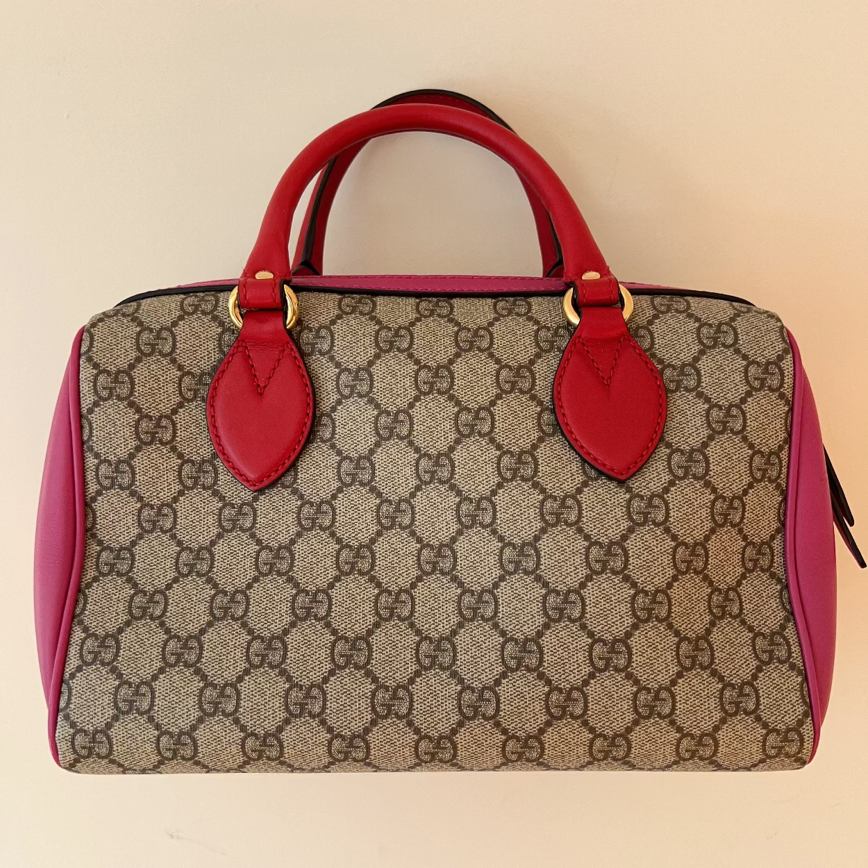 Designer handbag with red handles and trim on a beige background
