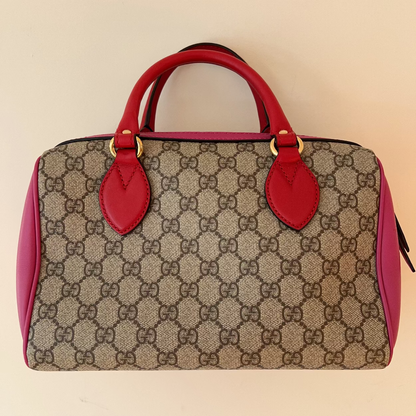 Designer handbag with red handles and trim on a beige background