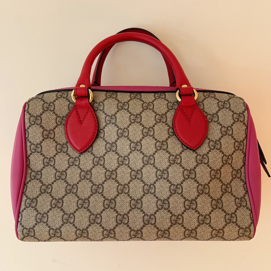 Designer handbag with red handles and trim on a beige background