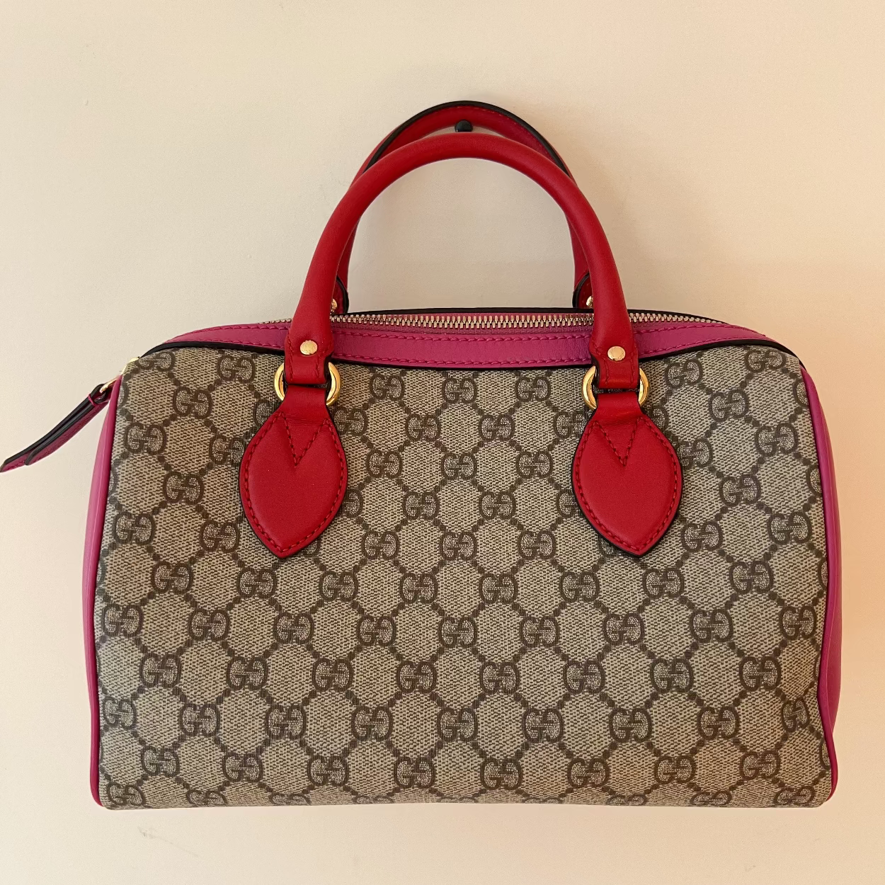 Designer handbag with red handles and accents on a beige background