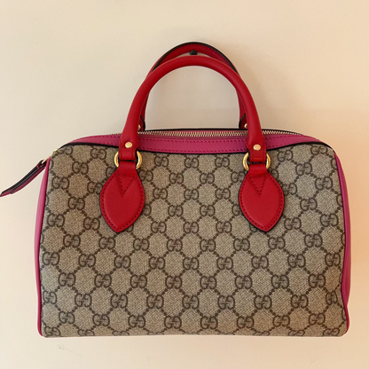 Designer handbag with red handles and accents on a beige background