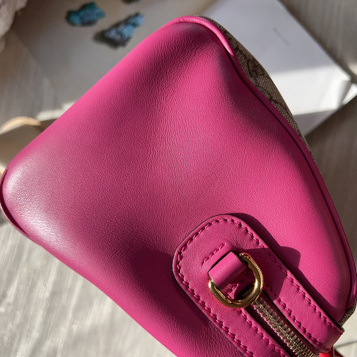 Pink leather handbag with gold clasp on a light wooden surface