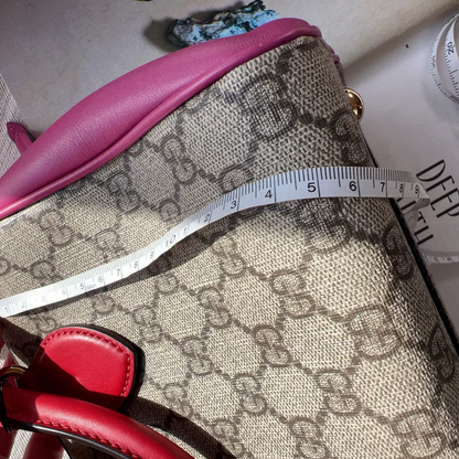 Handbag with pink top and red bottom section, featuring a pattern, held by a hand with a measuring tape on top.
