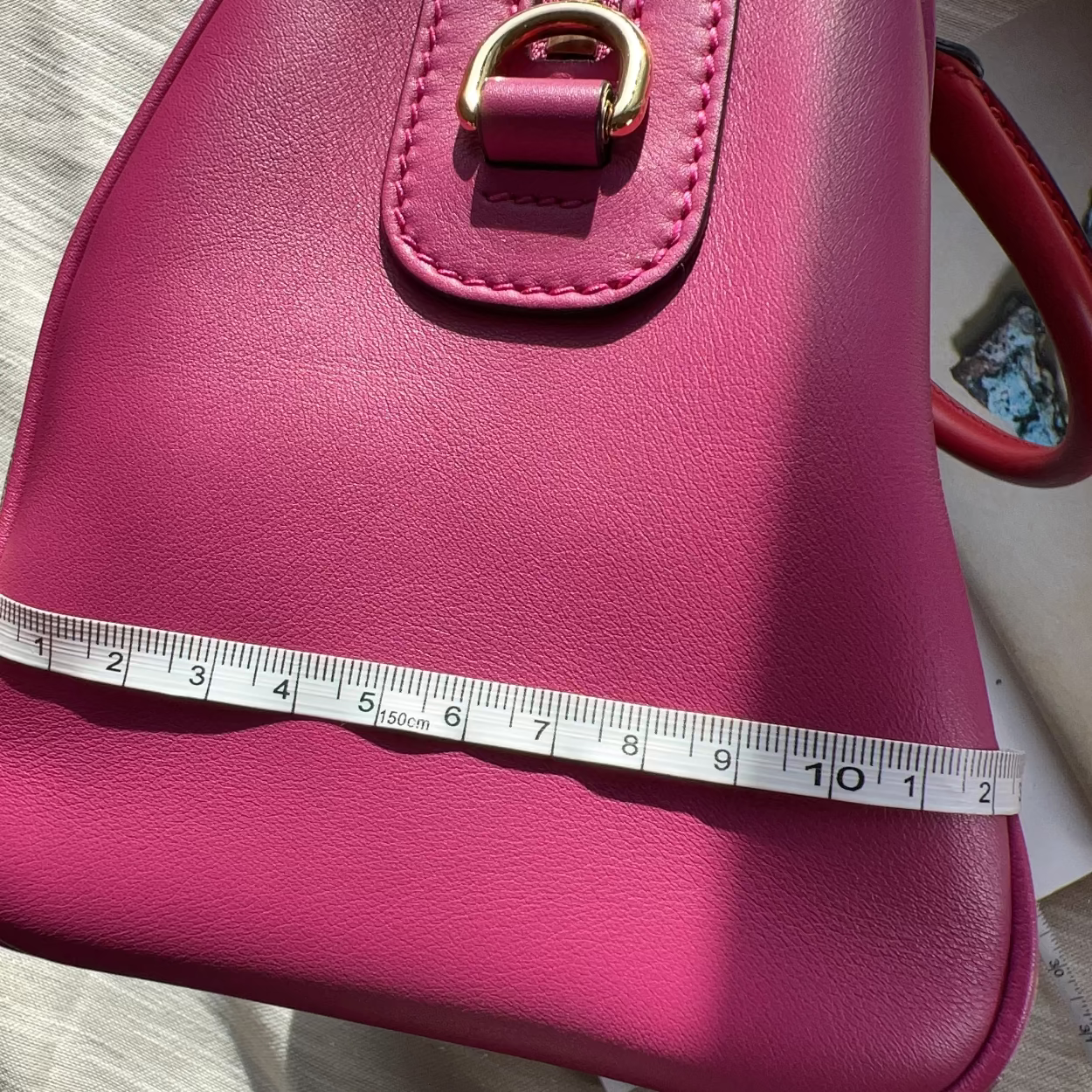 Pink handbag with a measuring tape for scale on a neutral background