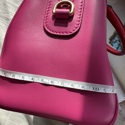 Pink handbag with a measuring tape for scale on a neutral background