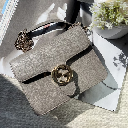 Gray handbag with a decorative clasp on a surface with a magazine and flowers.