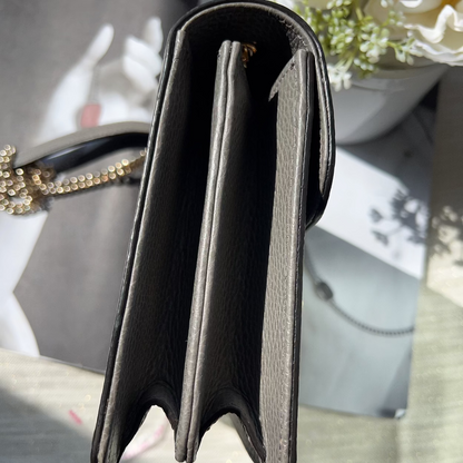 Black handbag with gold chain on a reflective surface