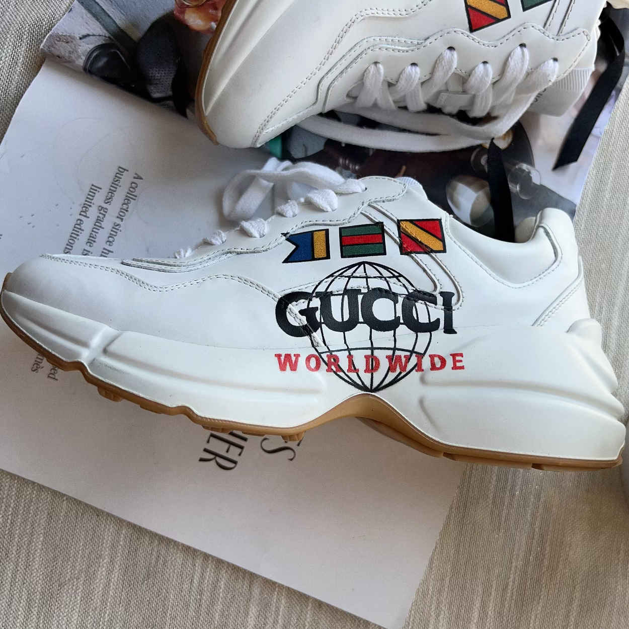 White Gucci sneaker with colorful logo on a surface with a magazine underneath