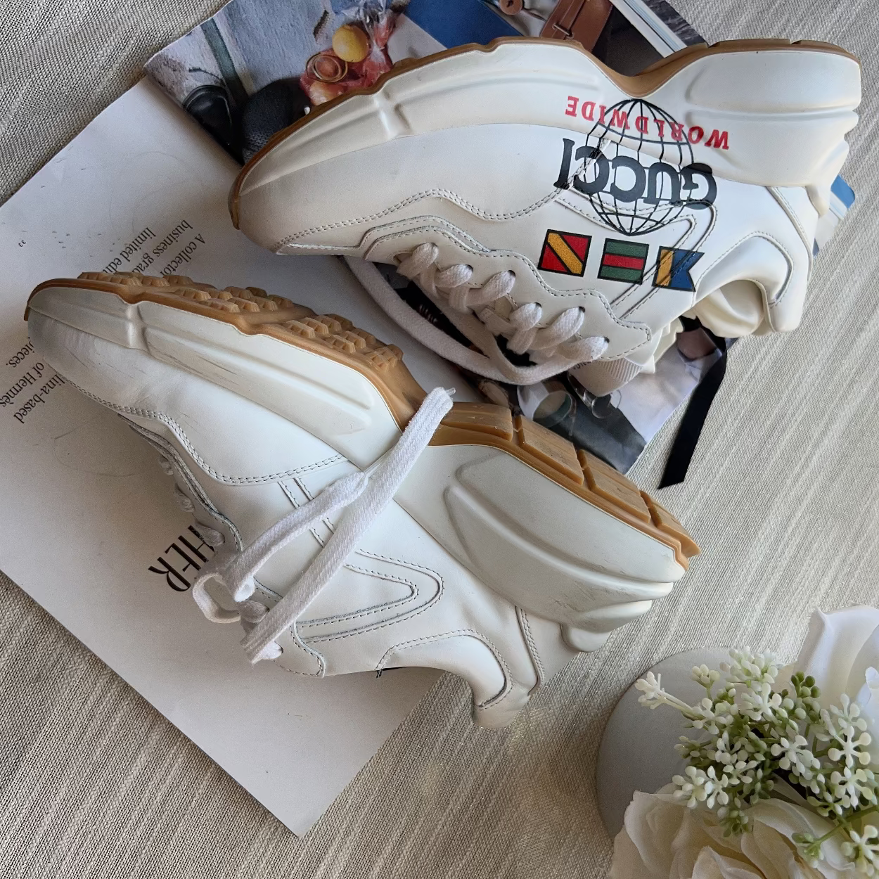 White sneakers with colorful text and designs on a surface with flowers and a magazine.