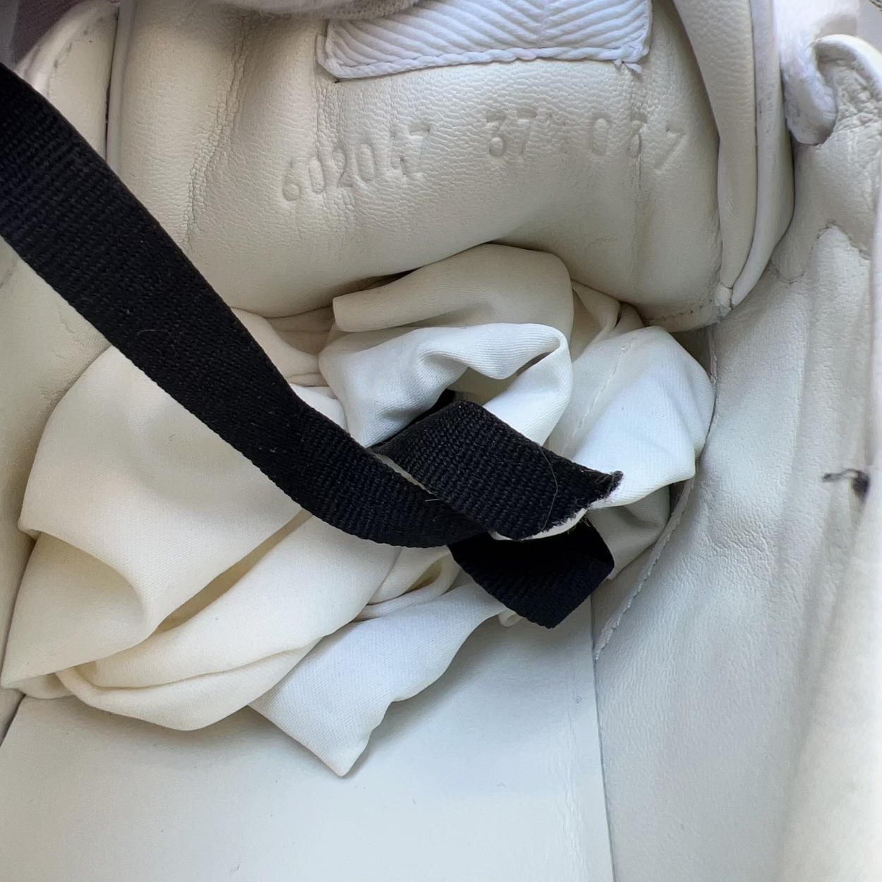 Close-up of a white shoe with a black strap and visible branding on a light background.