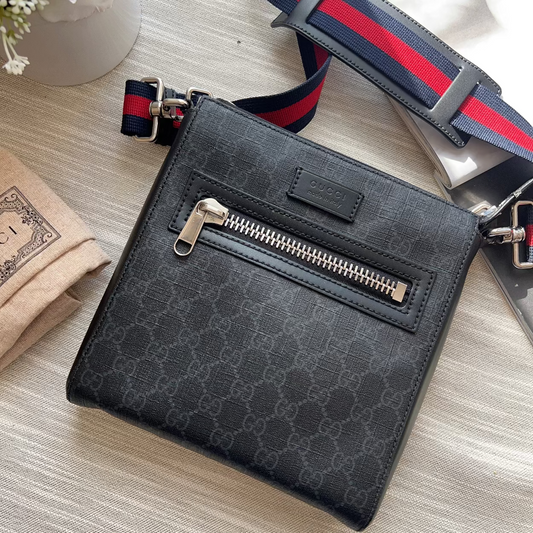 Black patterned crossbody bag with a visible brand logo on a light wooden surface.