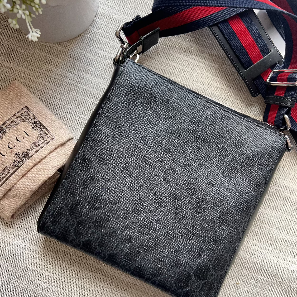 Black patterned crossbody bag with a red and blue strap on a light wooden surface.