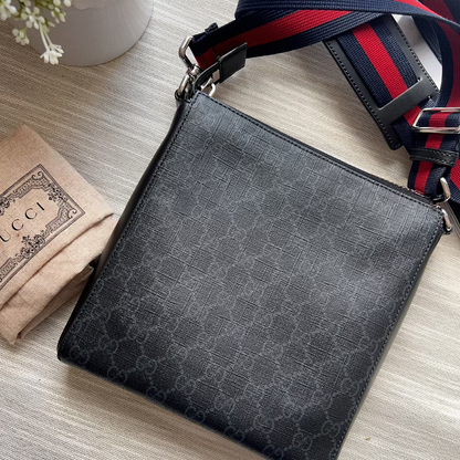 Black patterned crossbody bag with a red and blue strap on a light wooden surface.