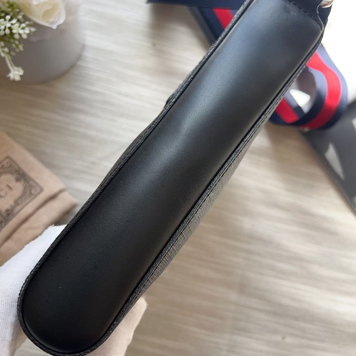 Black leather case on a light wooden surface with a striped strap in the background.