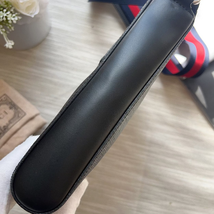 Black leather case on a light wooden surface with a striped strap in the background.