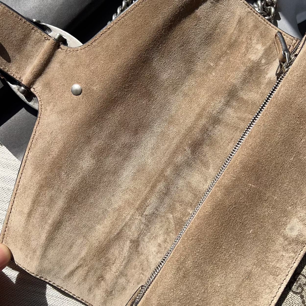 Close-up of a brown suede handbag with chain strap on a textured surface.