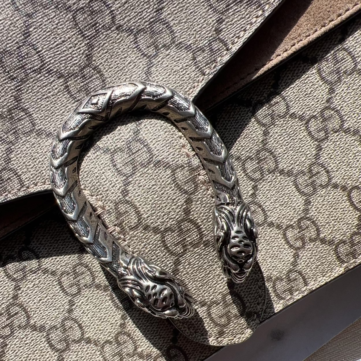 Silver bracelet with intricate design on a Gucci-patterned surface