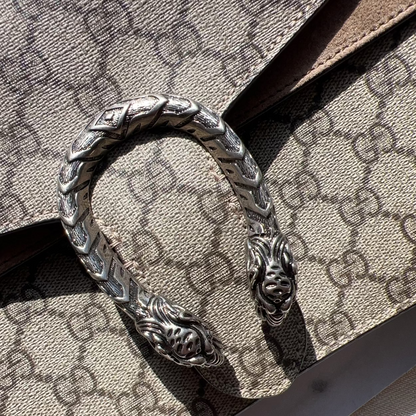 Silver bracelet with intricate design on a Gucci-patterned surface