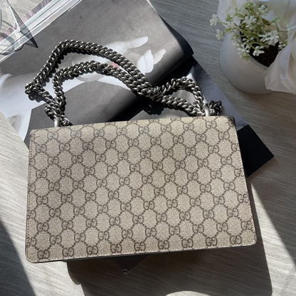 Designer handbag with chain strap on a textured surface with flowers in the background