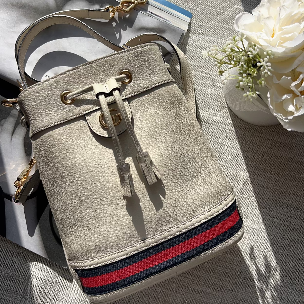 Beige handbag with red and blue stripe on a wooden surface with flowers in the background