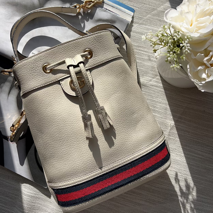 Beige handbag with red and blue stripe on a wooden surface with flowers in the background