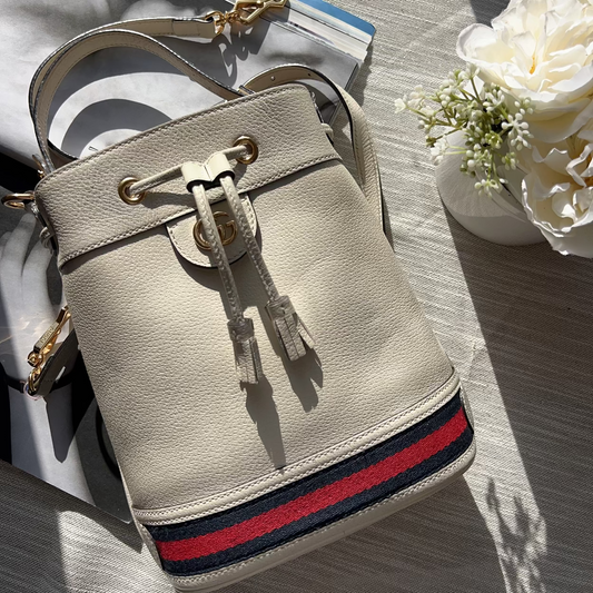 Beige handbag with red and blue stripe on a wooden surface with flowers in the background