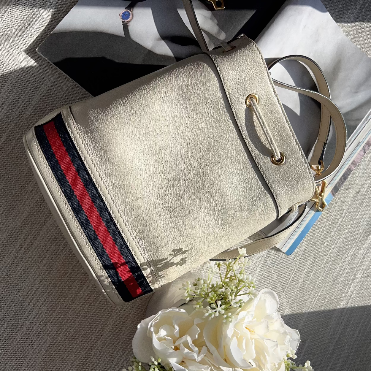 Beige handbag with red and blue stripe on a wooden surface with flowers