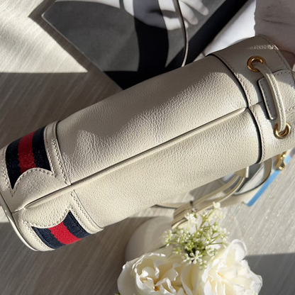Close-up of a cream-colored handbag with red and blue stripes, featuring a flower arrangement on a light background.