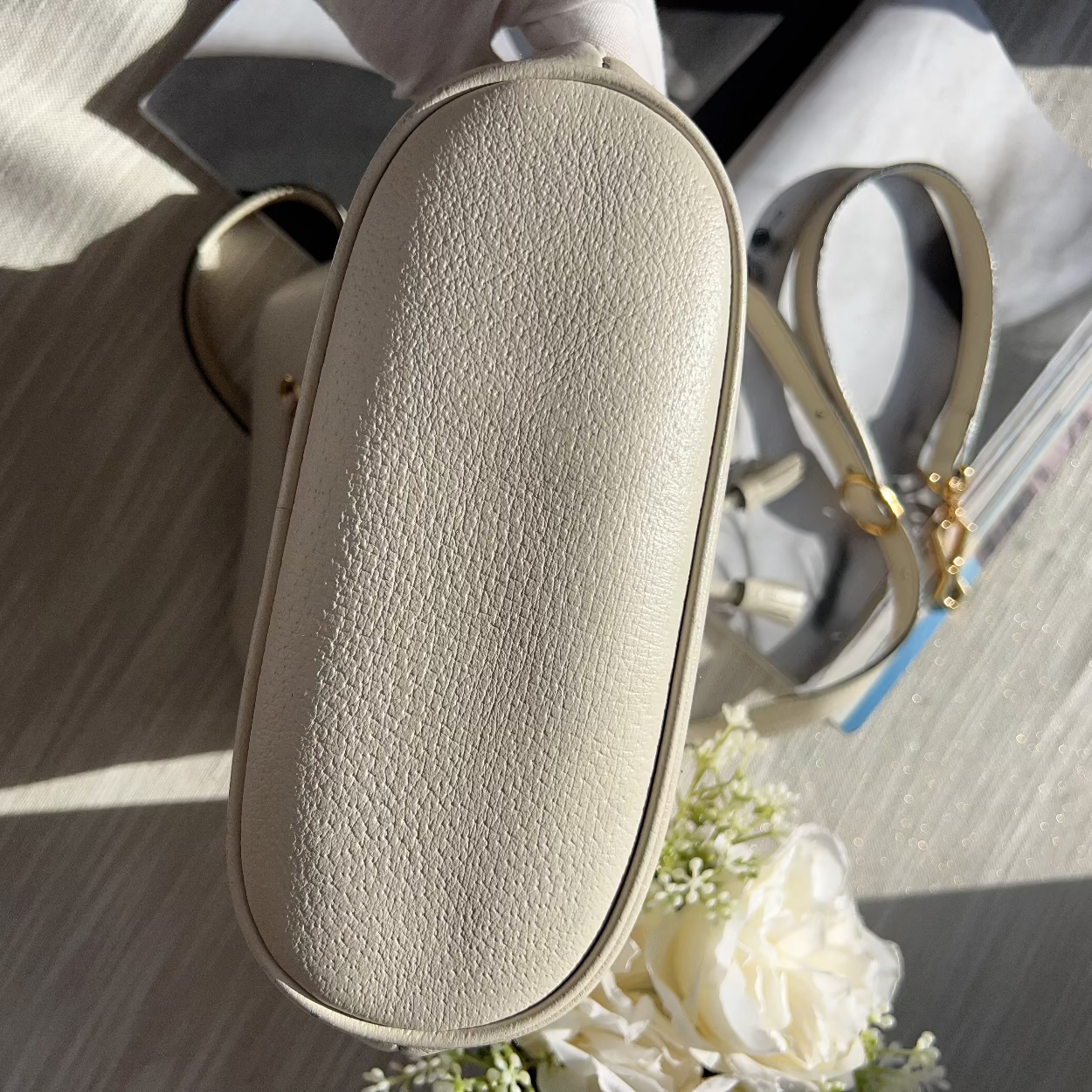 Beige textured handbag on a light wooden surface with white flowers.