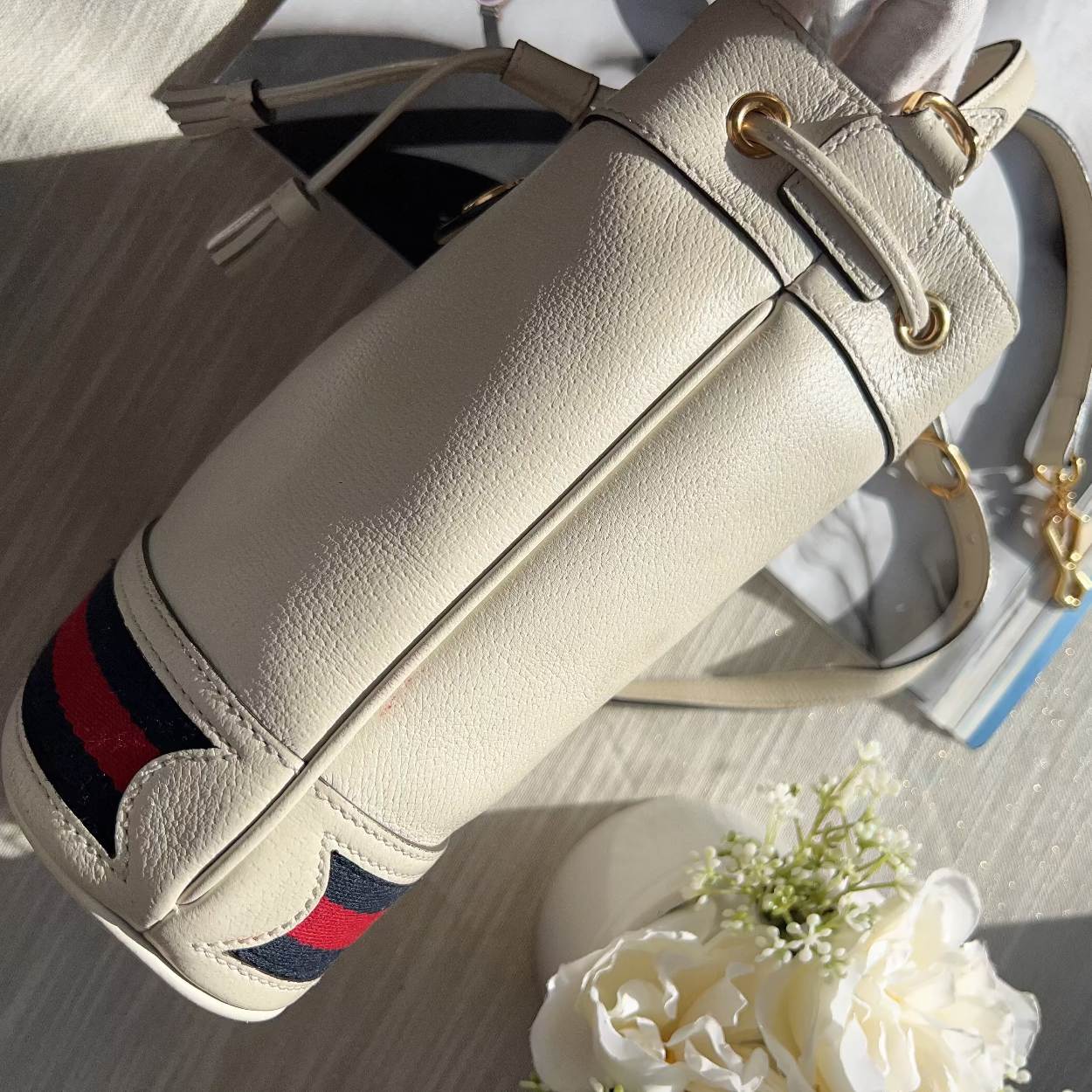 Beige handbag with red and blue stripes on a light surface with flowers